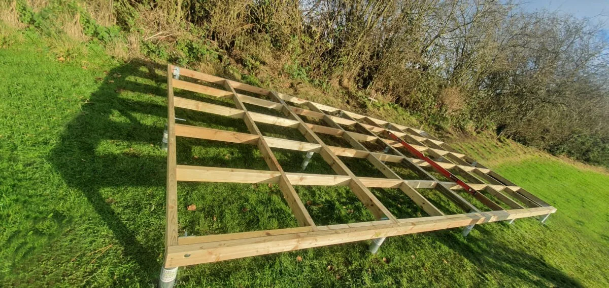 Timber foundation frame supported on ground screws on a grass slope