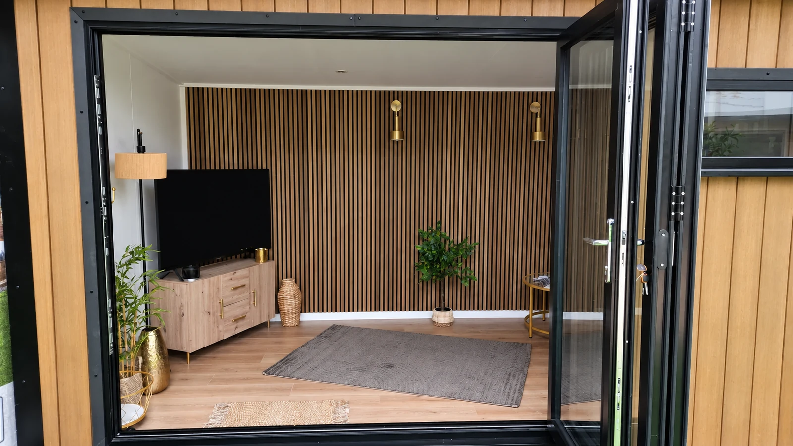 Showroom display room with bi-fold doors open onto a television and slatted timber wall